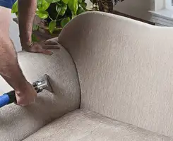 Professional upholstery cleaner deep-cleaning a fabric sofa with a handheld extraction tool and hose in Dover, DE.